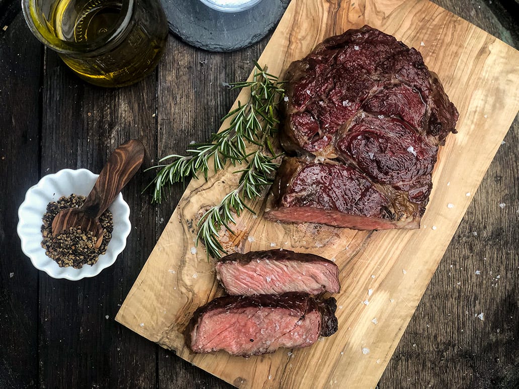 Saftiges, medium gegrilltes Rindersteak, aufgeschnitten auf einem rustikalen Holzbrett mit Rosmarin und Gewürzen angerichtet.