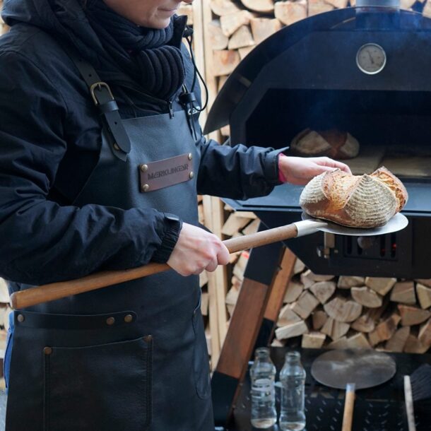 Person mit Leder-Schürze entnimmt mit MERKLINGER Brotschieber ein frisch gebackenes Brot.“