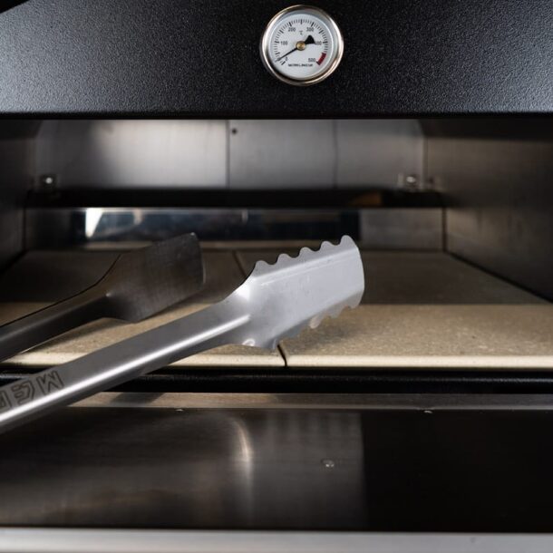  „MERKLINGER Grillzange auf dem Schamottstein vor dem Backraum, Thermometer im Hintergrund.“