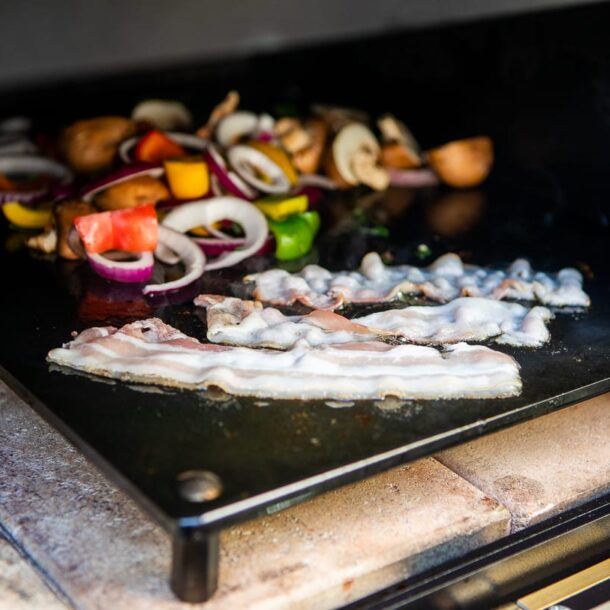 Baconstreifen und buntes Gemüse auf der erhöhten Plancha im Merklinger Holzbackofen.