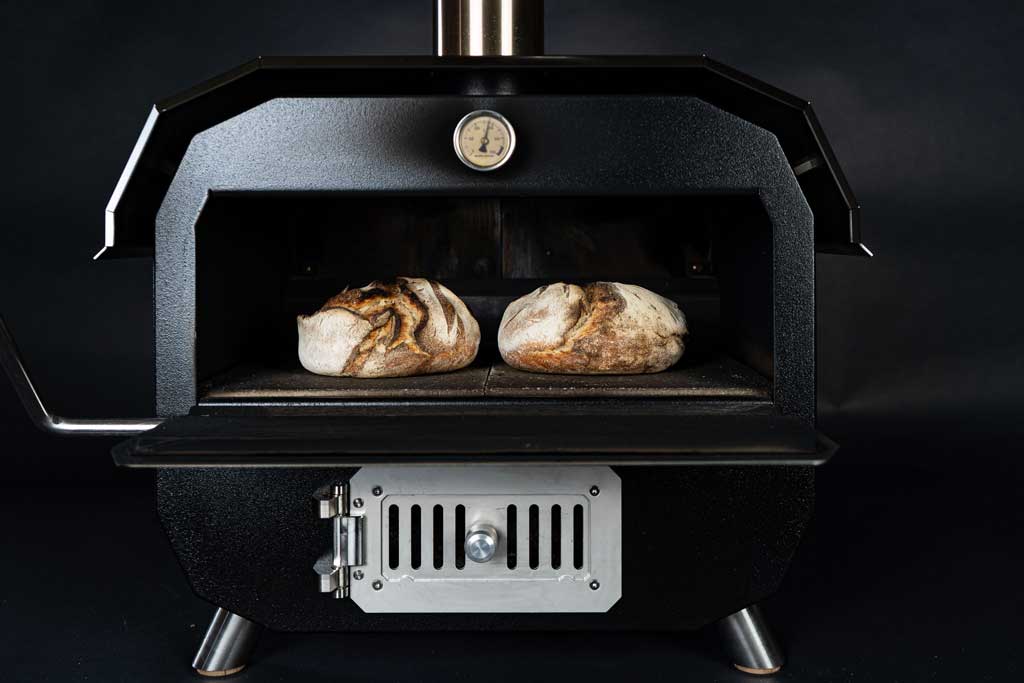 Zwei frisch gebackene Brote stehen auf Schaufel im MERKLINGER Holzbackofen