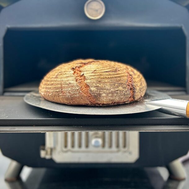 „Rundes Landbrot auf Brotschieber vor dem MERKLINGER Holzbackofen – knusprige Kruste frisch gebacken.“