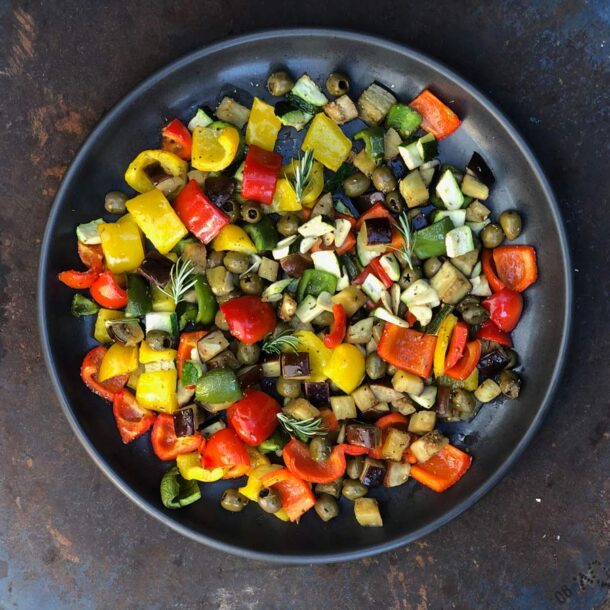 Nahaufnahme einer runden Ofenplatte mit bunt gewürfeltem Ofengemüse – Paprika in Rot/ Gelb/ Grün, Zucchini, Aubergine und Oliven – garniert mit Rosmarin und Knoblauch Merklinger Zubehör Denkkeramik Keltenschale 01